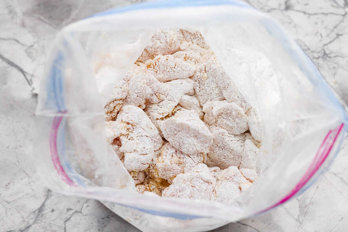 Bite sized pieces of chicken covered in cornstarch in a ziplock bag.