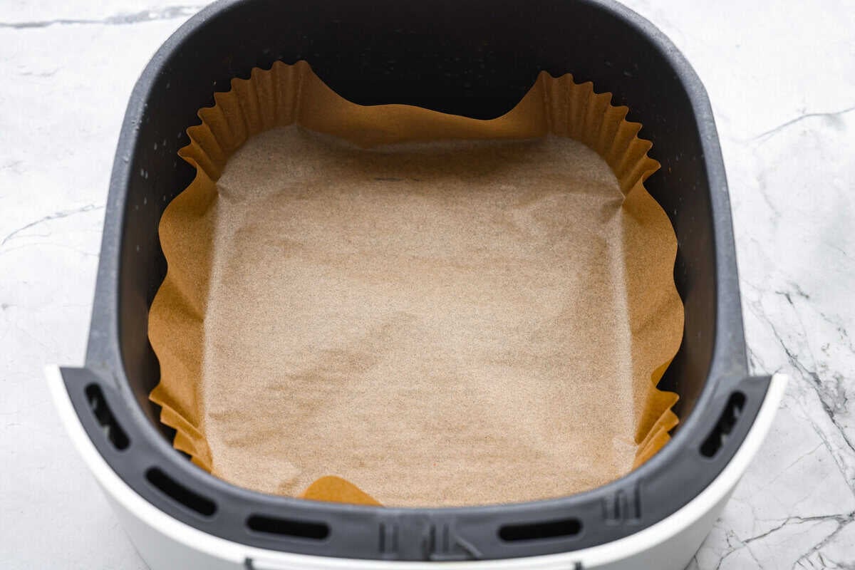 Air fryer basket with and air fryer parchment liner in it.