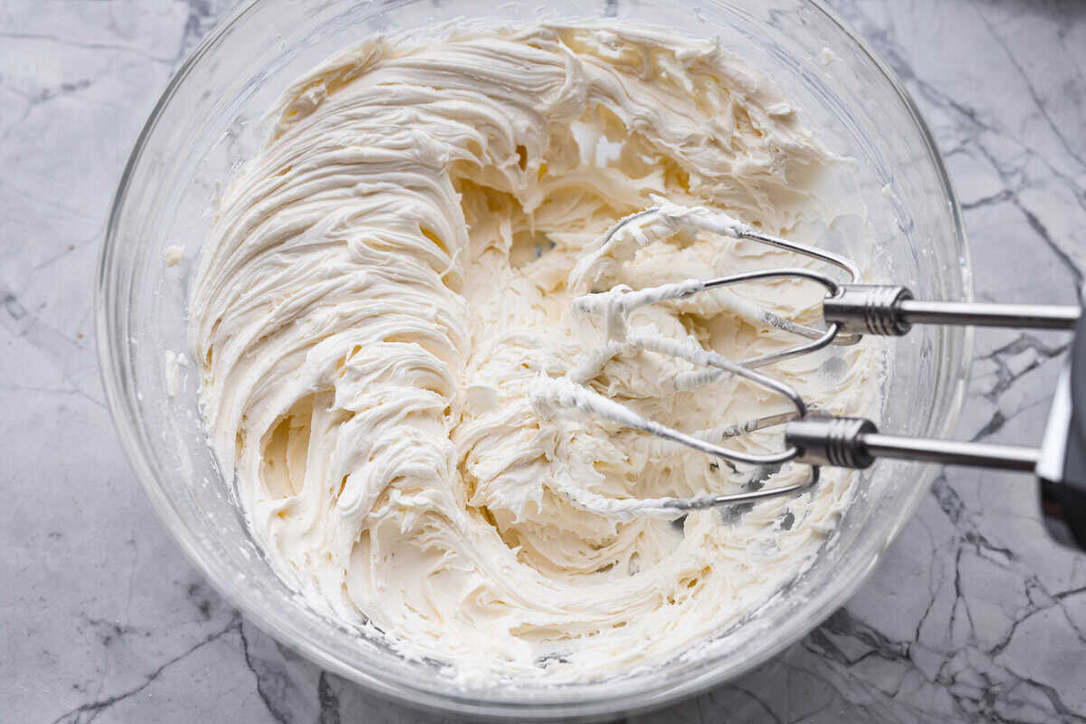 Frosting ingredients being whipped with a hand mixer until fluffy.