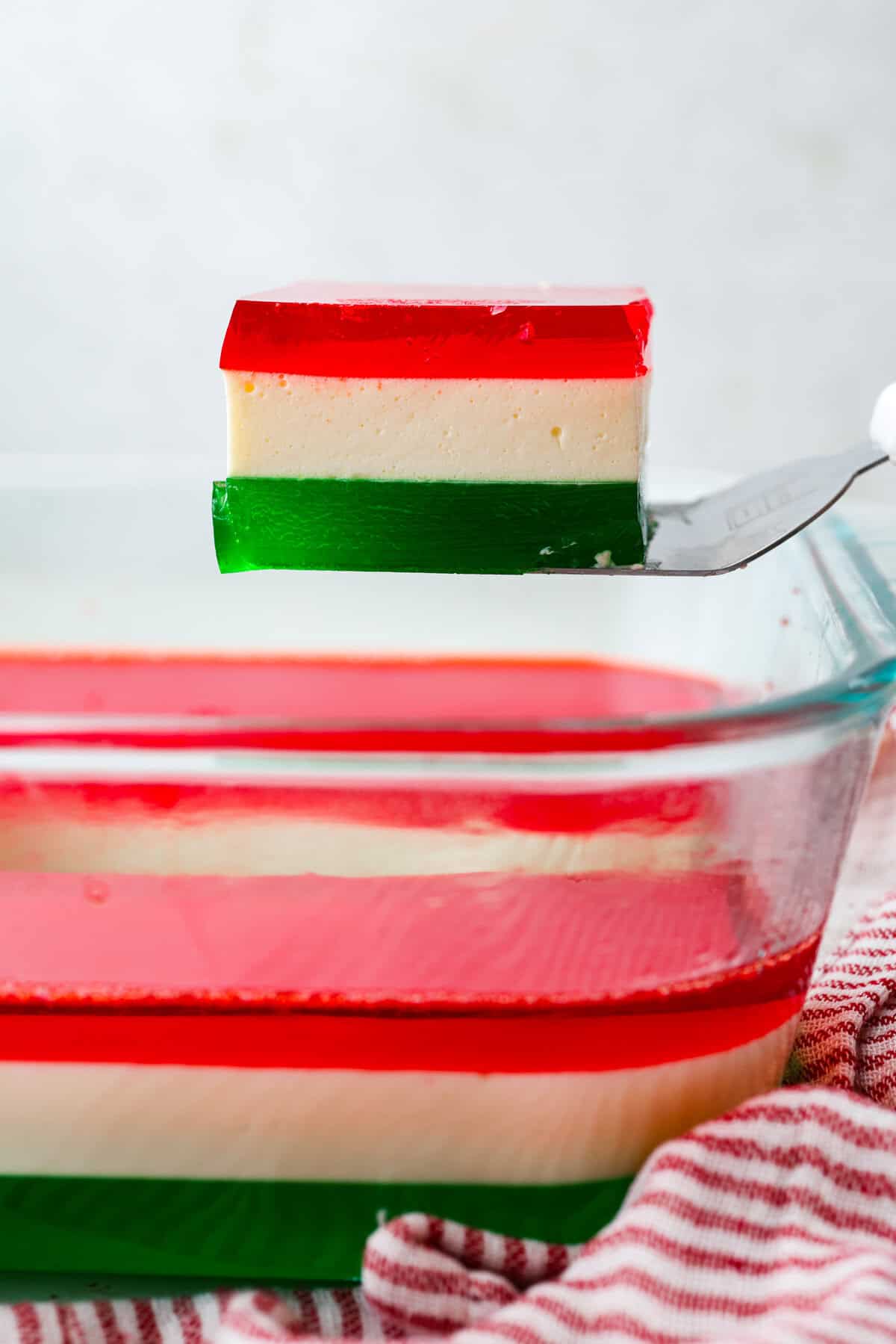 Someone lifting a serving of Christmas ribbon salad out from the baking dish.