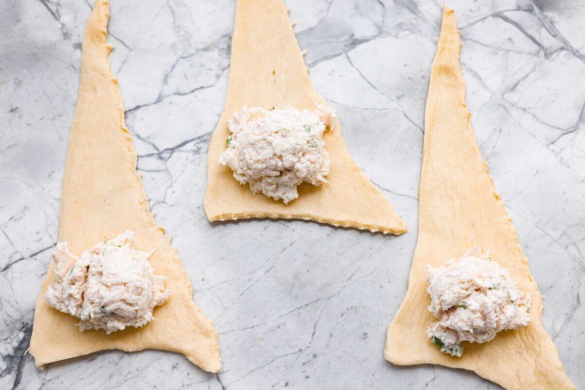 Crescent roll triangles separated and spread out with a dollop of chicken mixture scooped onto the wide end. 