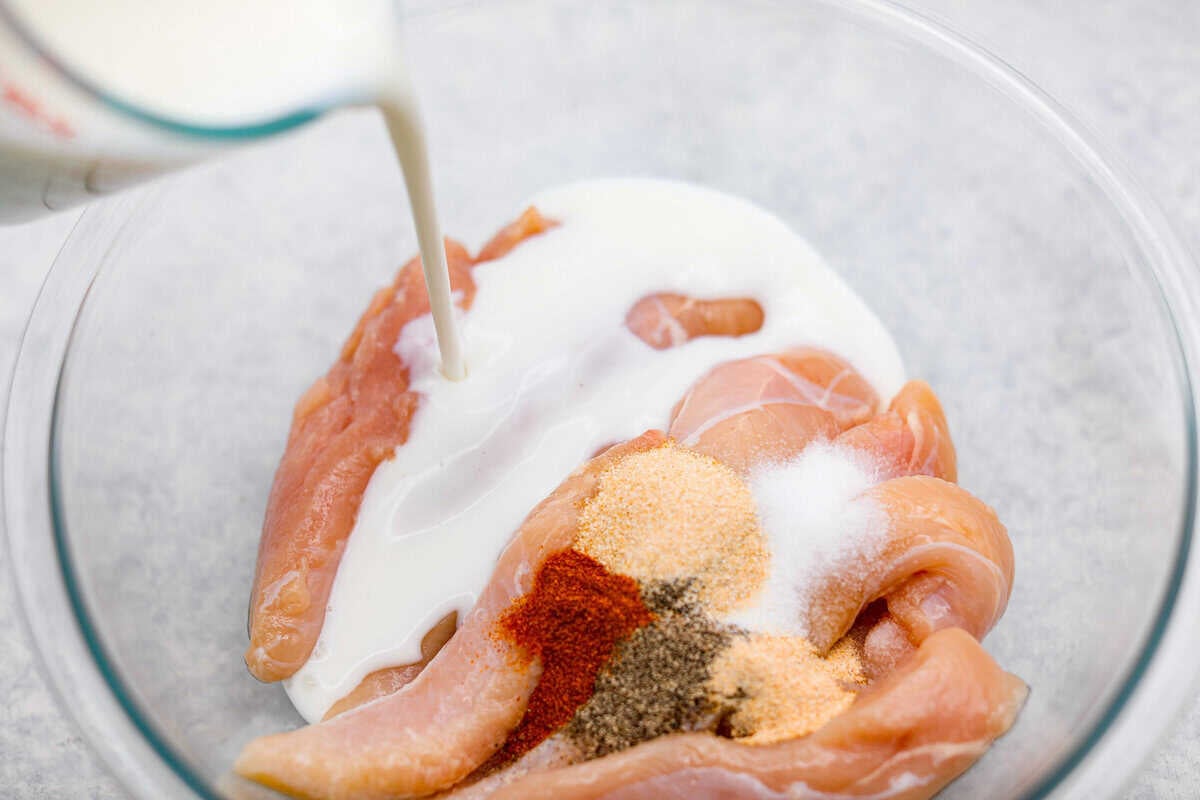 Chicken tenders, buttermilk and seasonings added to a mixing bowl.