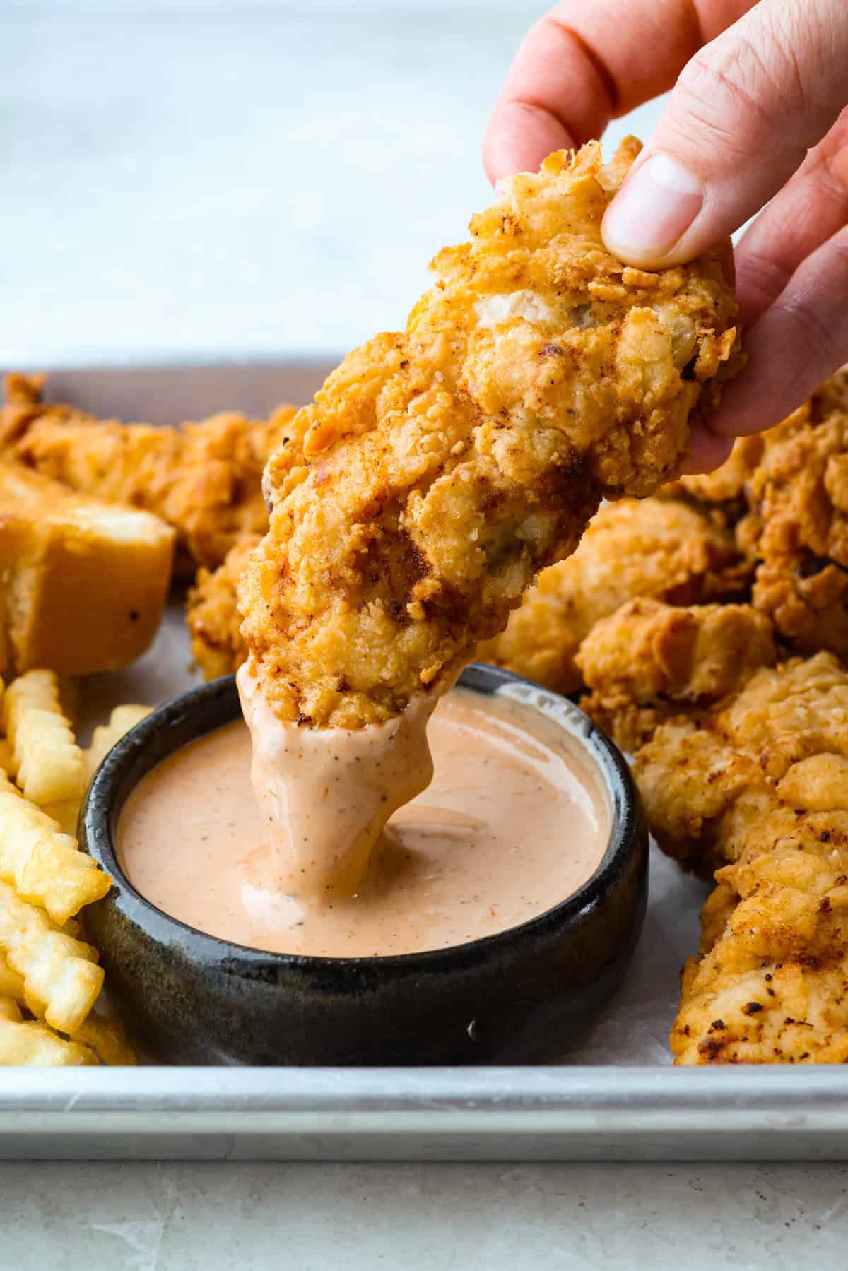 Someone dipping a Raising Cane's chicken into a small bowl of Cane's sauce.