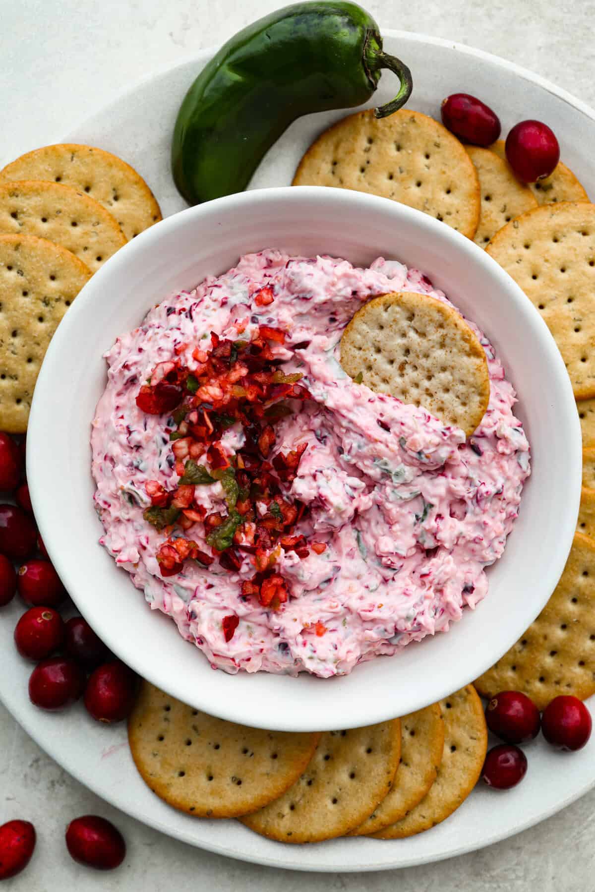 Bowl of cranberry jalapeño dip surrounded by crackers, cranberries and jalapeños.