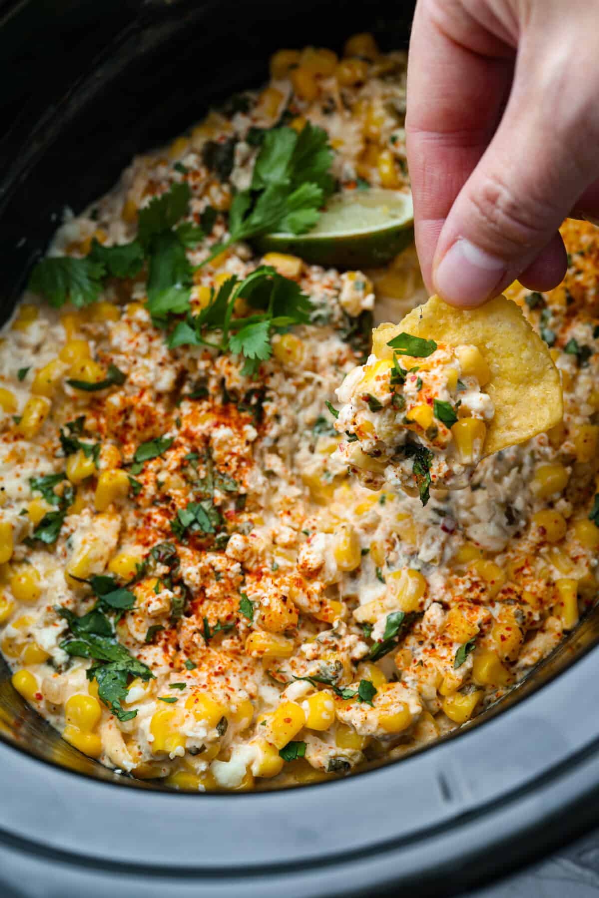 Someone scooping a portion of Mexican street corn dip with a chip.