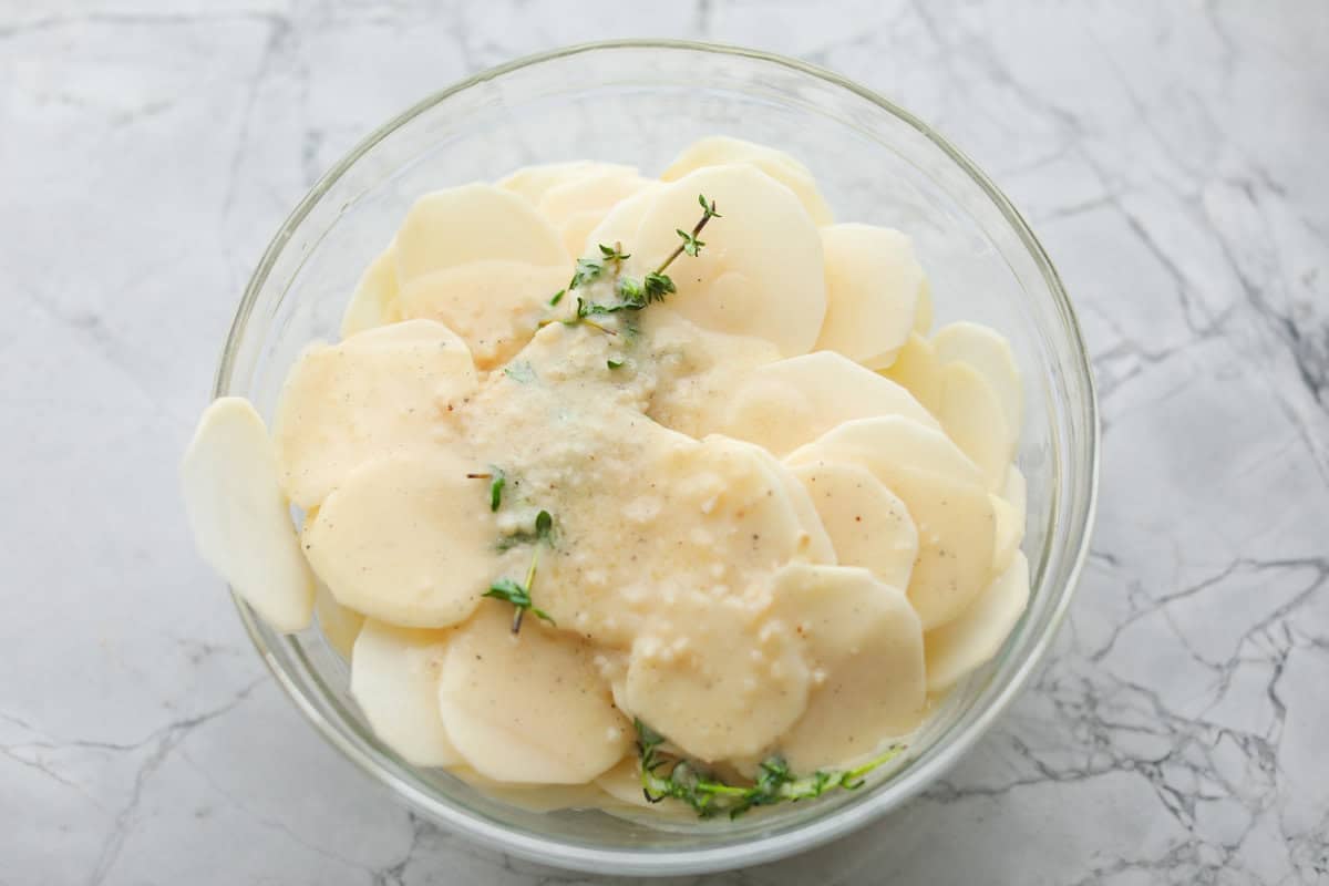 Thinly sliced potatoes in a bowl covered in butter mixture.