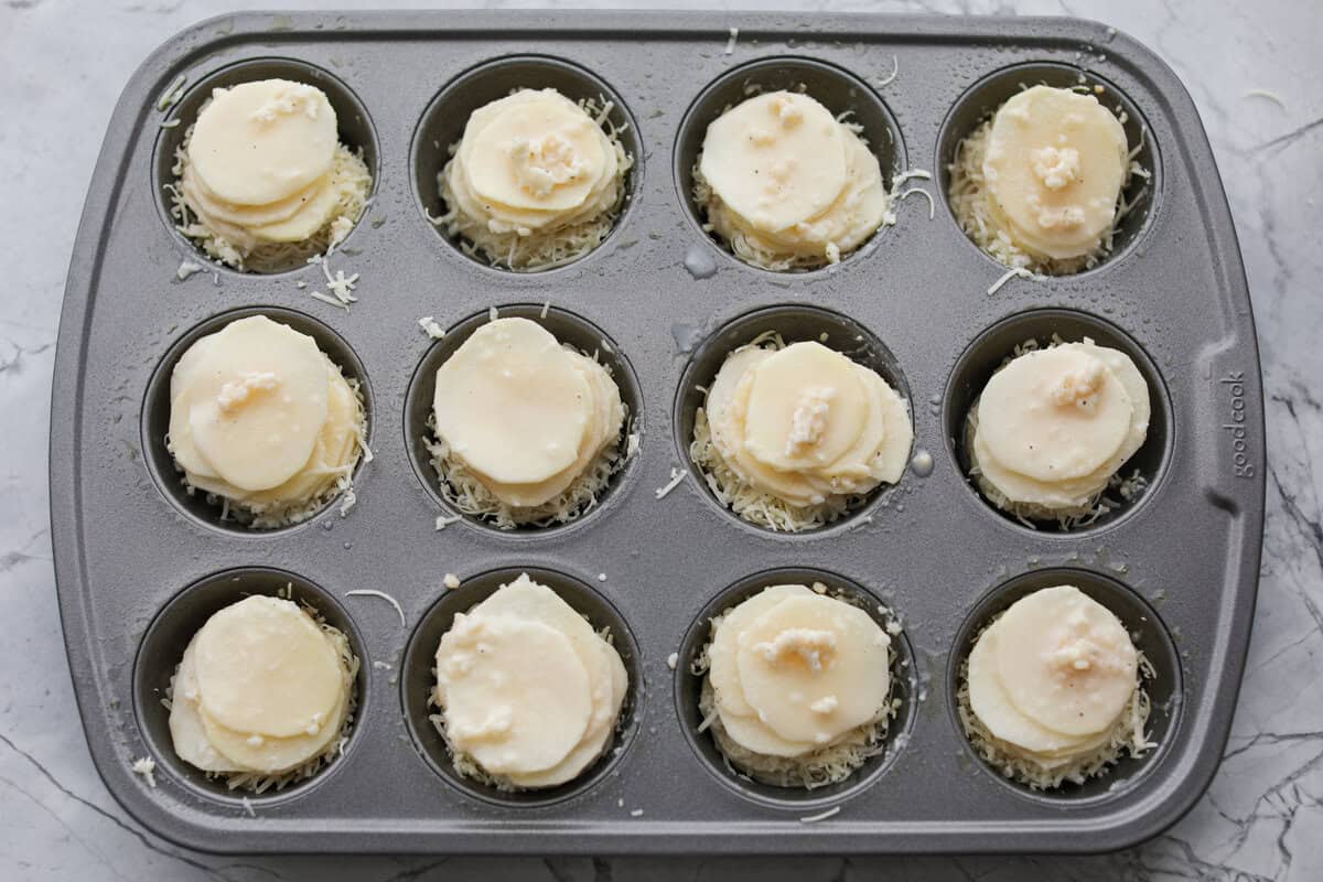 Potato slices stakced in a muffin tin with the butter sauce and cheese in between the layers.