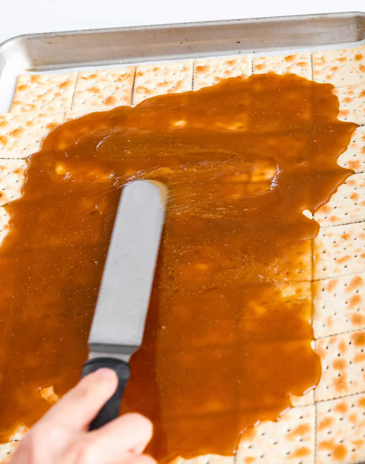 Someone gently spreading toffee over the saltine crackers.