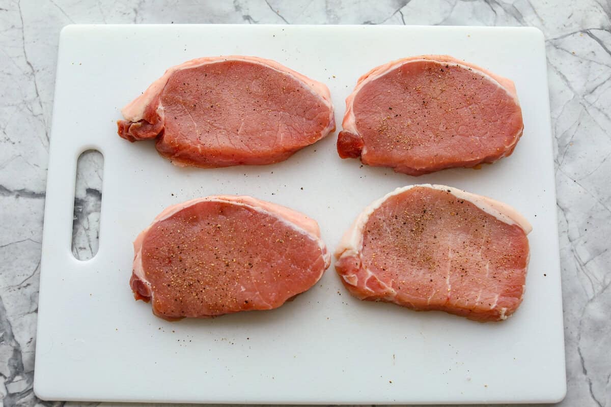 Pork chops seasoned and resting on a cutting board.