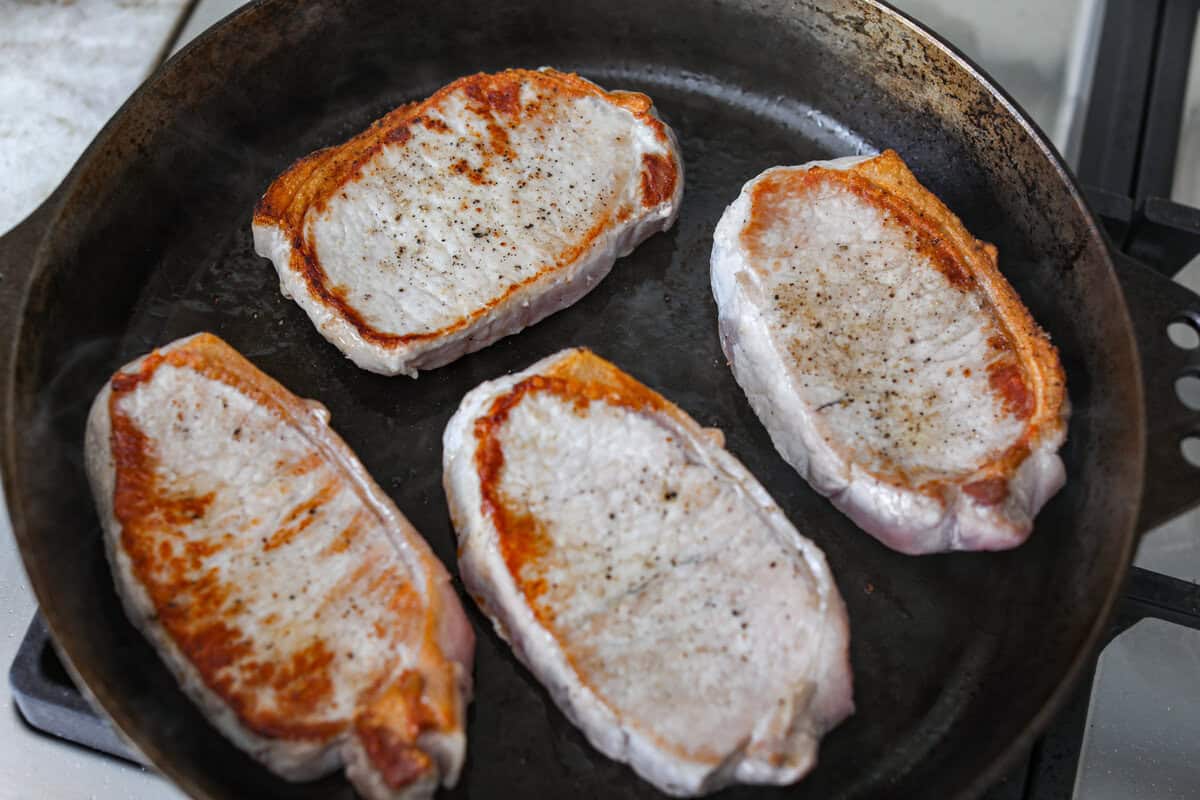 Seasoned pork chops being seared in a skillet.