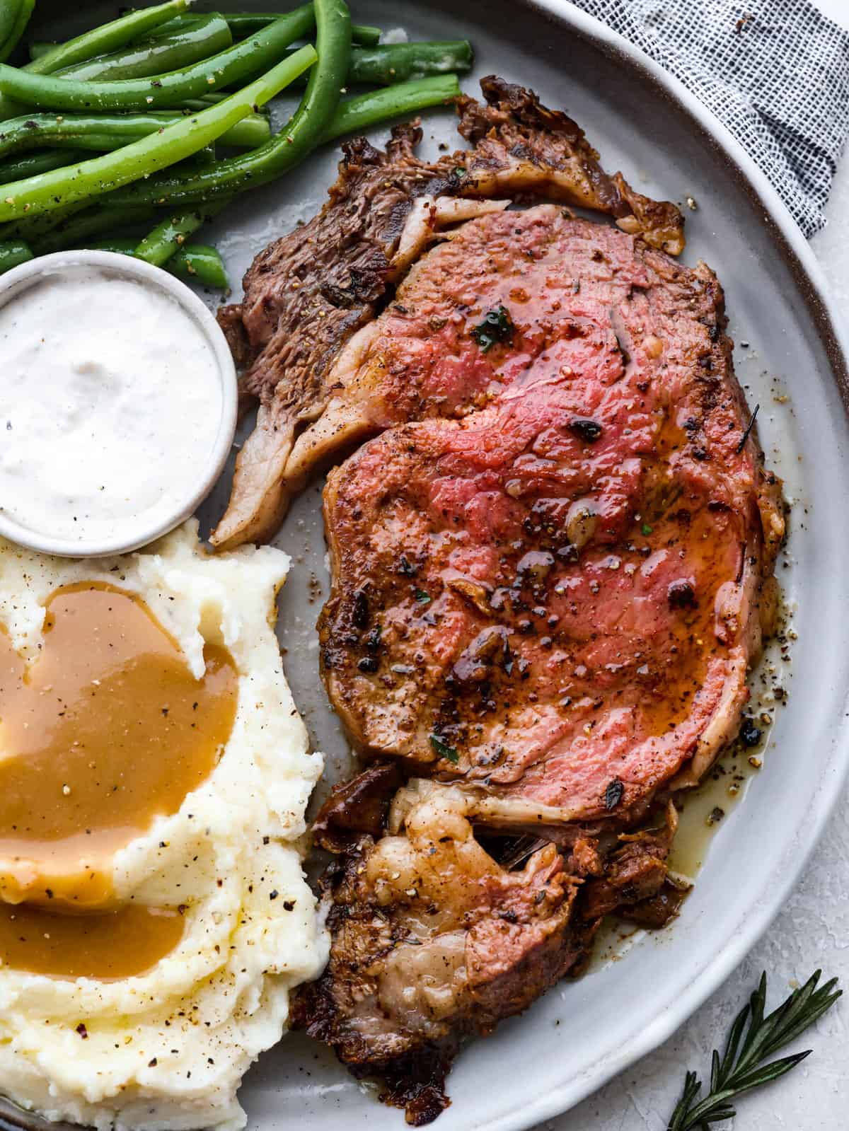 Plated slice of prime rib next to a horseradish cup, green beans, and mashed potatoes and gravy. 