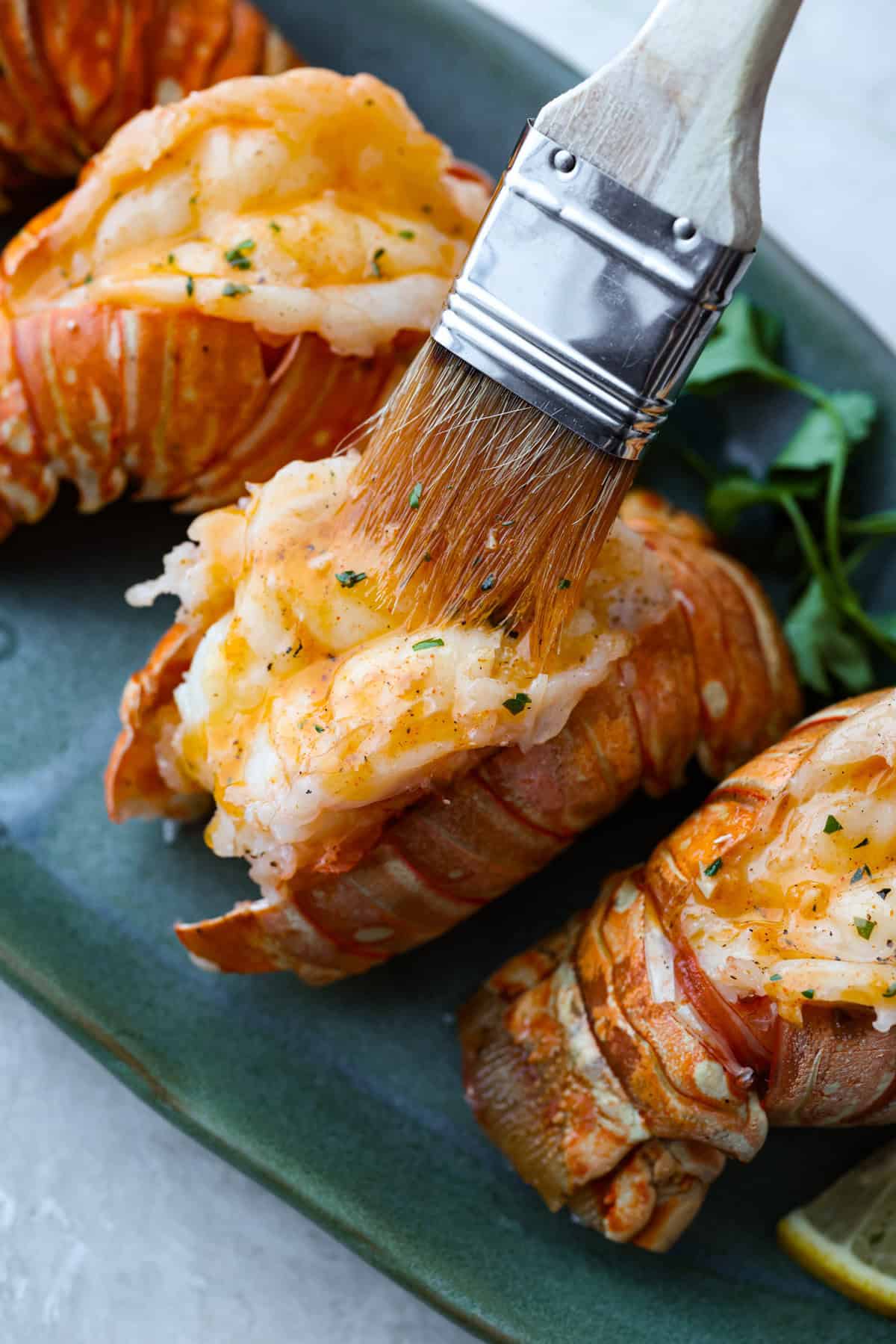 Someone spreading the herbed butter over the cooked tails.