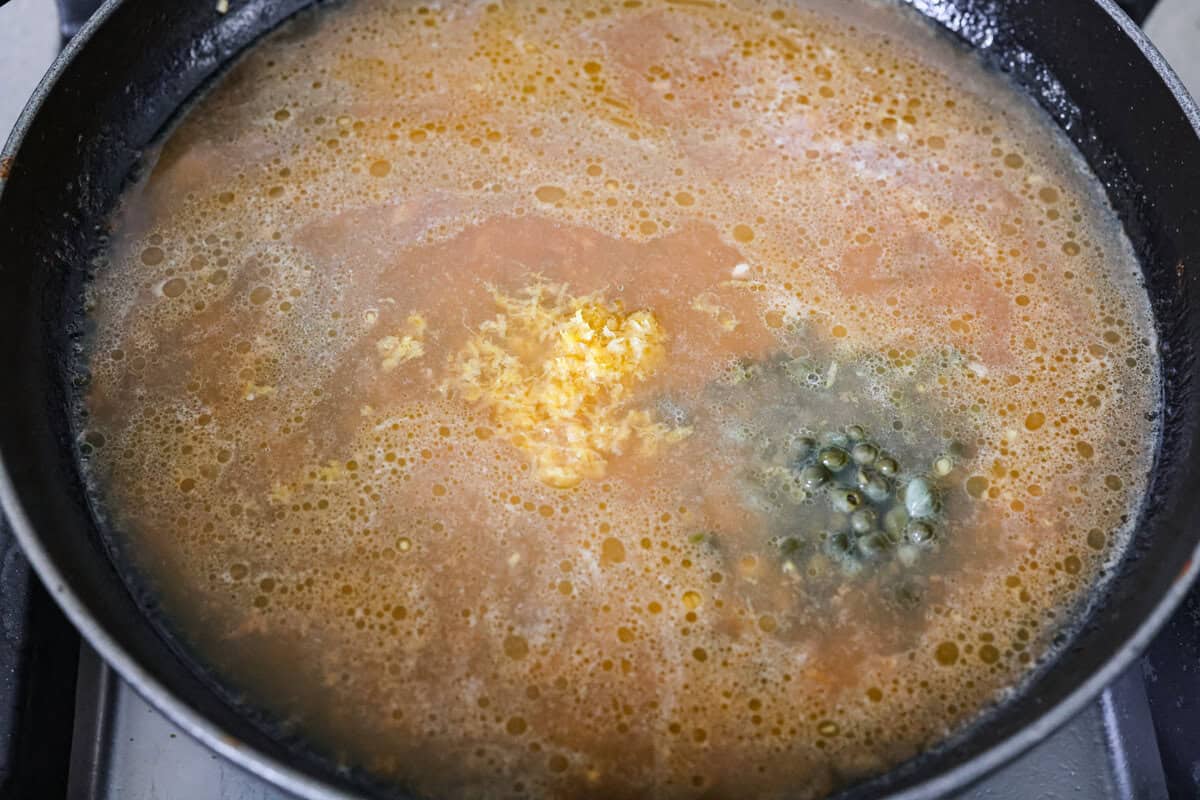 Chicken broth, lemon zest, lemon juice, and capers added to the skillet to simmer and reduce.