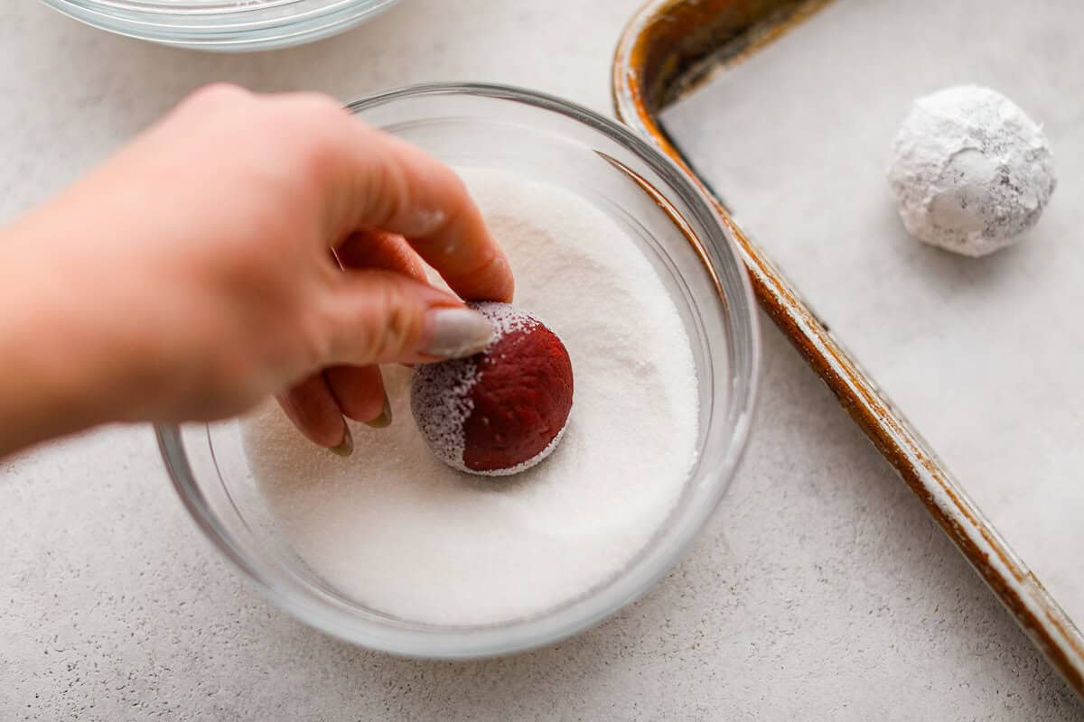 Someone rolling the cookie dough ball in a bowl of granulated sugar.