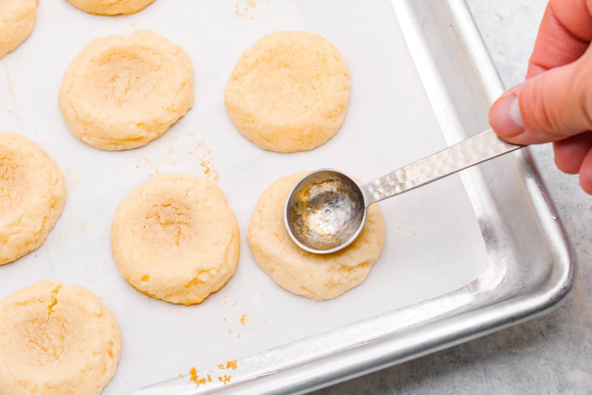 Someone pressing the teaspoon into the baked cookies.