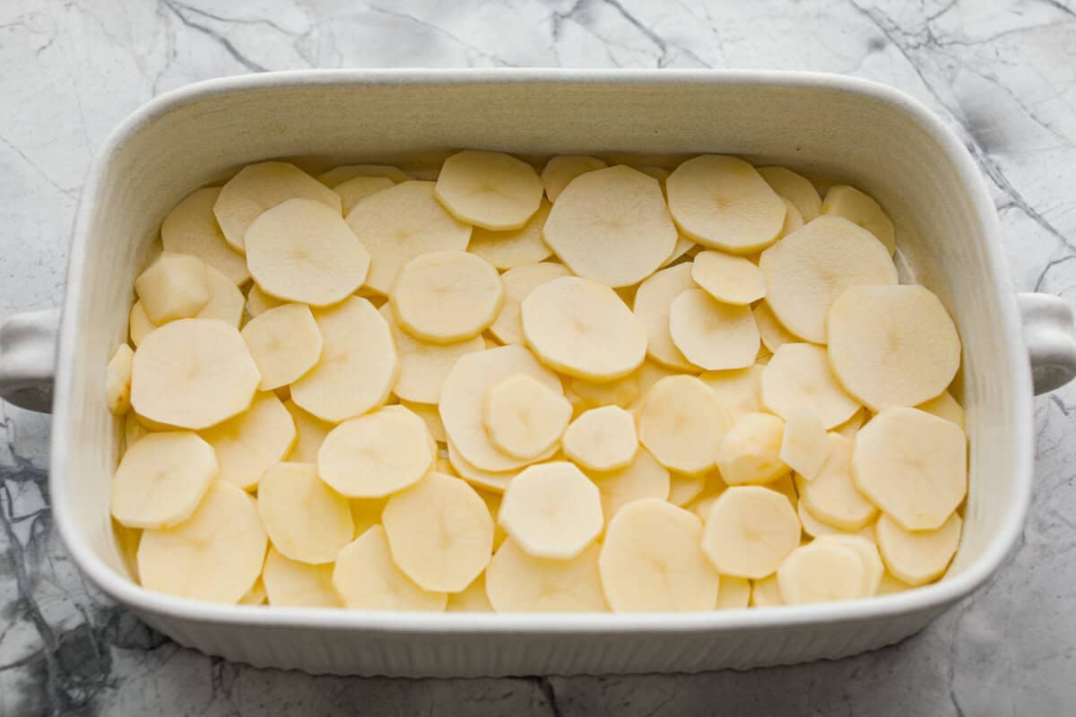 Sliced potatoes layered on the bottom of the baking dish.